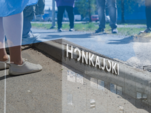 Honkajoki-kyltti sekä ulkona seisovia ihmisiä aurinkoisena päivänä.